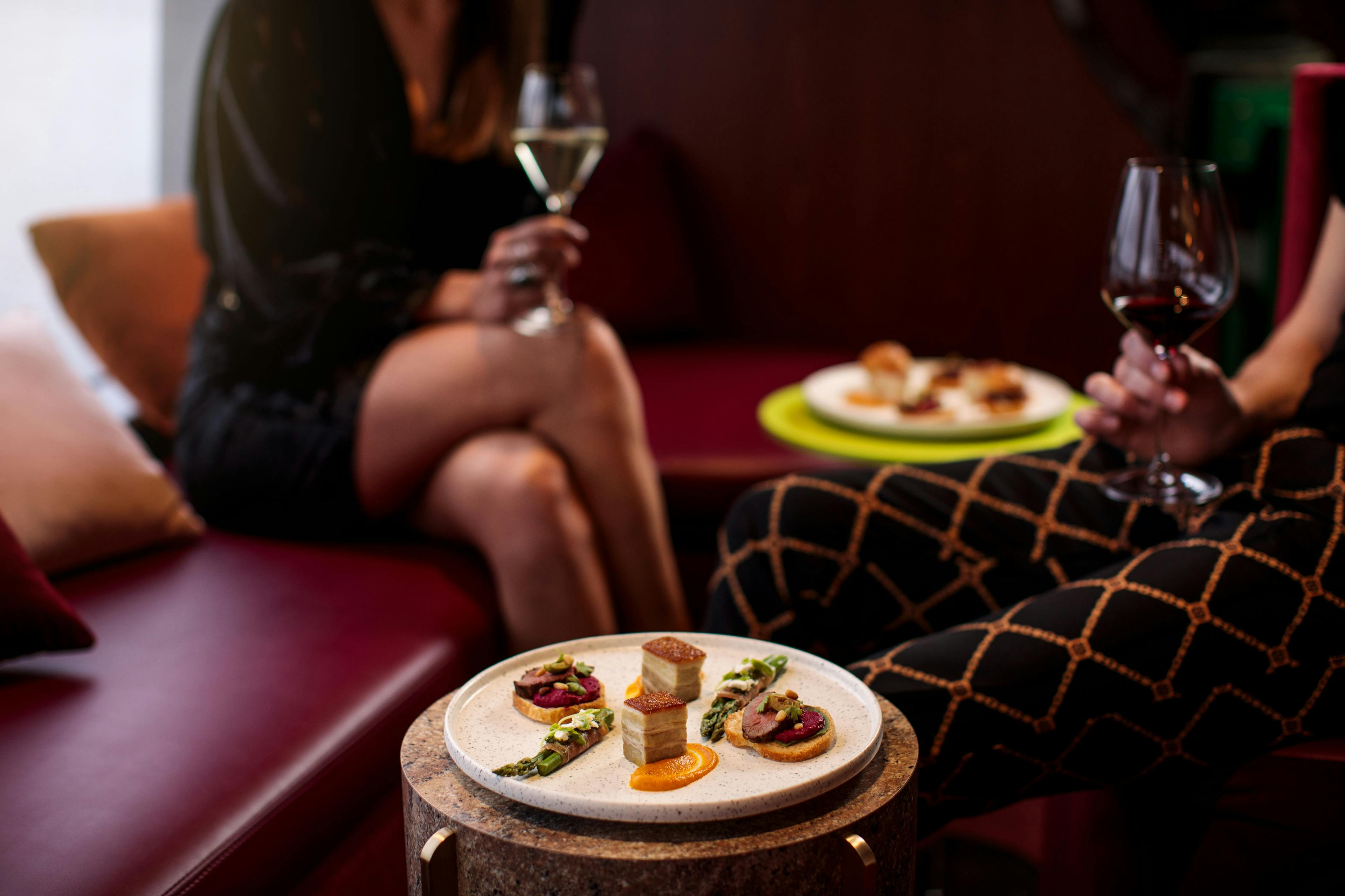 Two people drinking red wine sit on board the Mona Ferry Posh Pit with tiny but delectable food sitting in front of them.