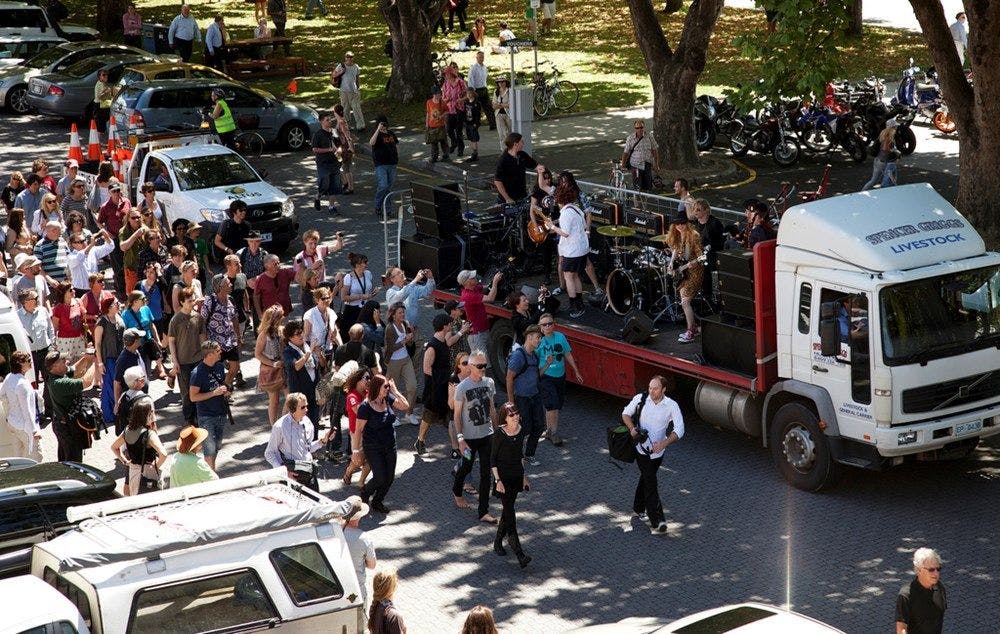 A band on the back of a truck plays as a crowd walks by.