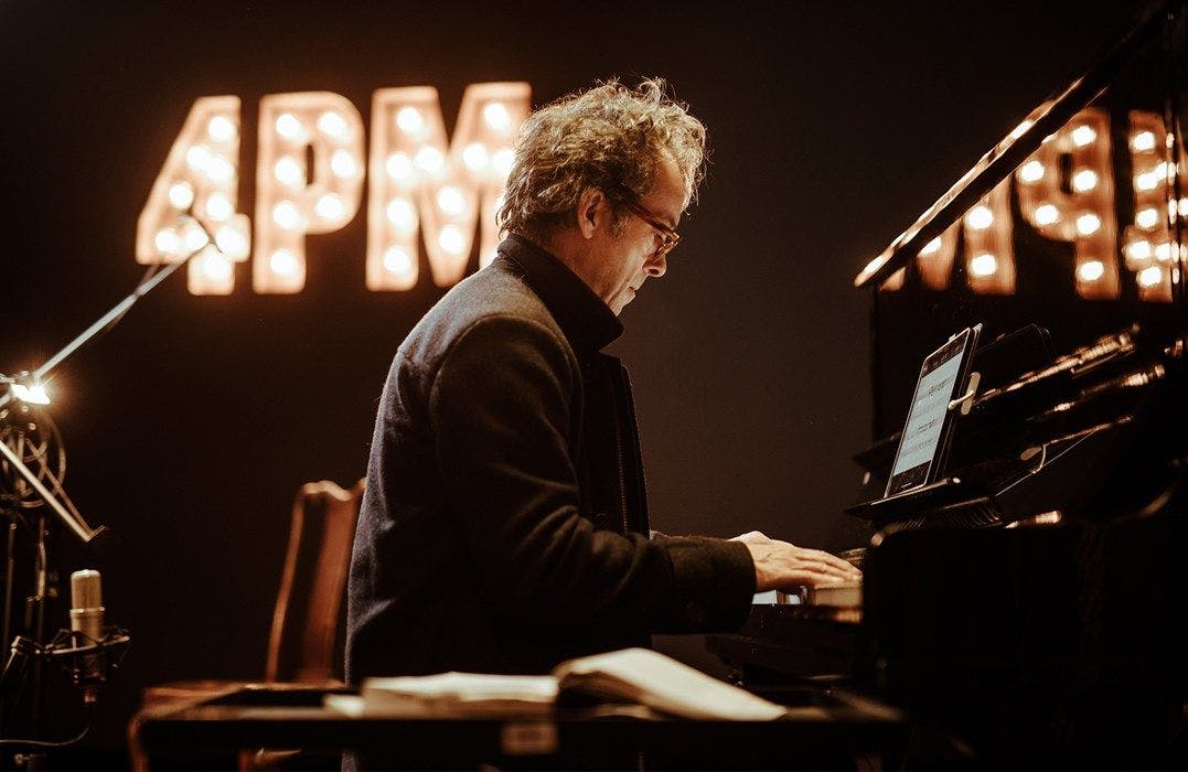 Dean Stevenson plays the Piano under a sign displaying 4PM in lights