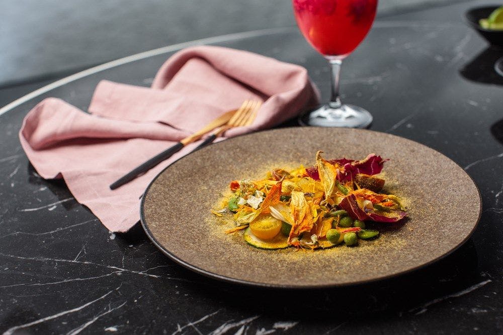 A plate with yellow tinged vegetables on a dark marble table with blush pink linen napkin.