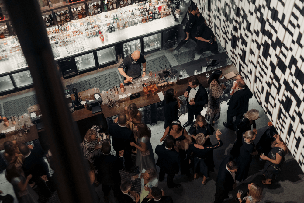 Birds eye view of people gathering at the bar while a staff member pours cocktails