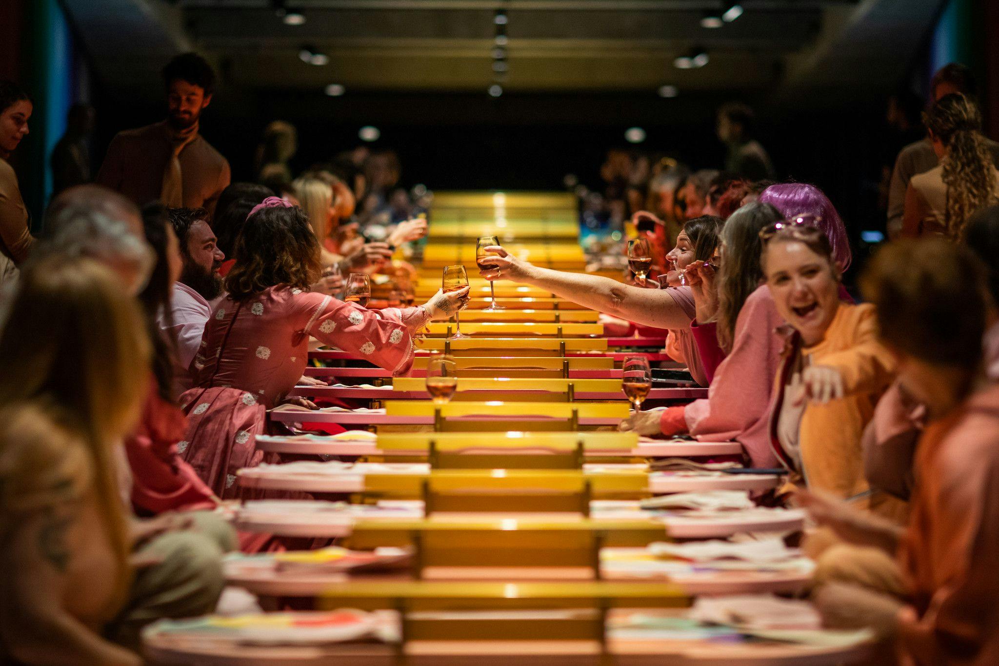 A colourful long table seated with equally colourfully dressed people.