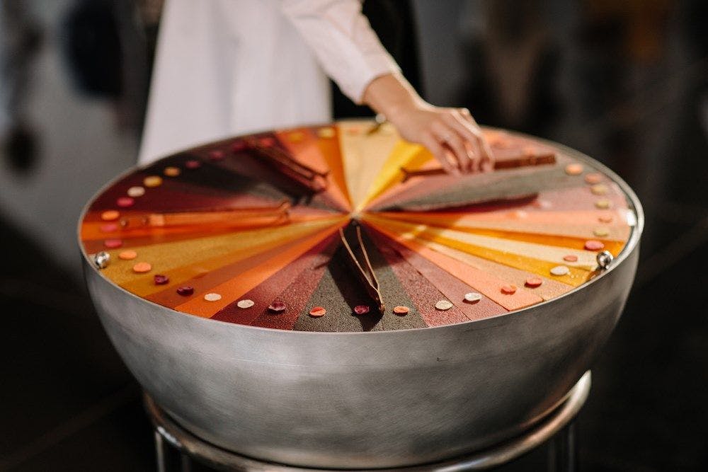 A hand moves across a large steel drum with a felt autumnal coloured gradient ontop.